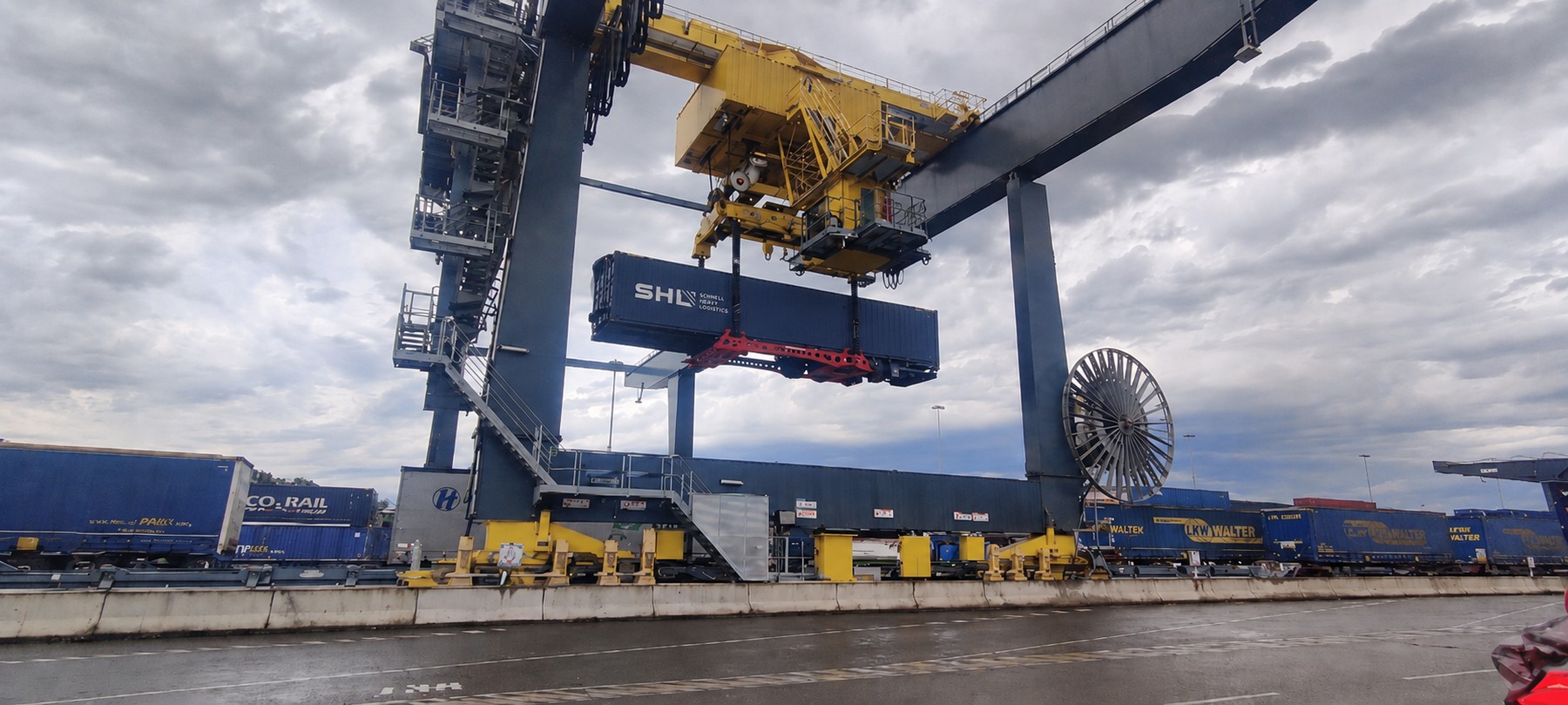 SHL Intermodal terminal — crane lifting navy SHL semitrailer onto rail wagon